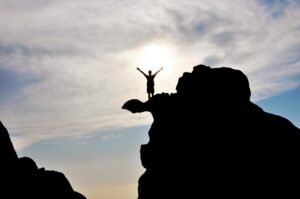 Silhouette of a person celebrating on a mountain peak against a dramatic sky, symbolizing freedom and success.